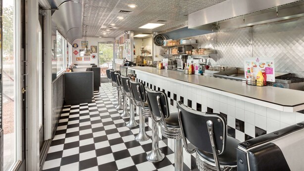 A diner with a checkered floor, bar stools, and a counter with food items.