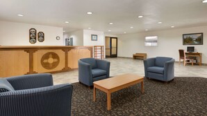 A lobby with a reception desk, two blue armchairs, a wooden coffee table, and a carpeted floor.