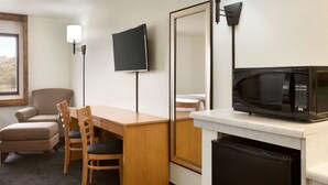 A hotel room with a wooden desk, two chairs, a television, a microwave, and a refrigerator.