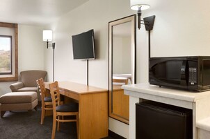 Quarto de hotel com escrivaninha de madeira, duas cadeiras, televisão, micro-ondas e frigorífico.