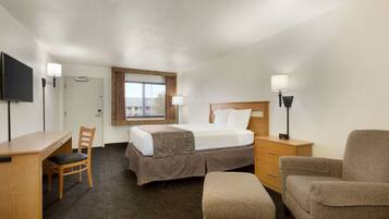 A hotel room with a bed, desk, chair, and a television.