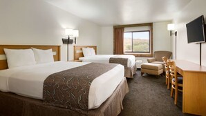 A hotel room with two beds, a desk, a chair, a TV, and a window with a view.