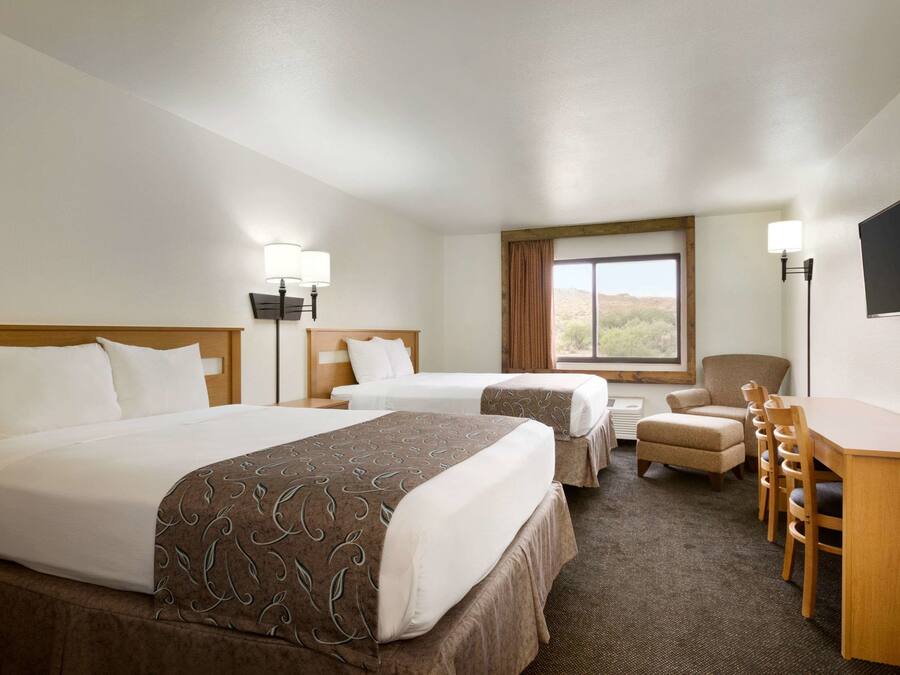 A hotel room with two beds, a desk, a chair, a TV, and a window with a view.
