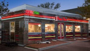 A diner with a neon sign, a drive-up window, and a red awning.