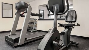 Une salle de sport équipée d’un tapis de course, d’un vélo elliptique et de poids.