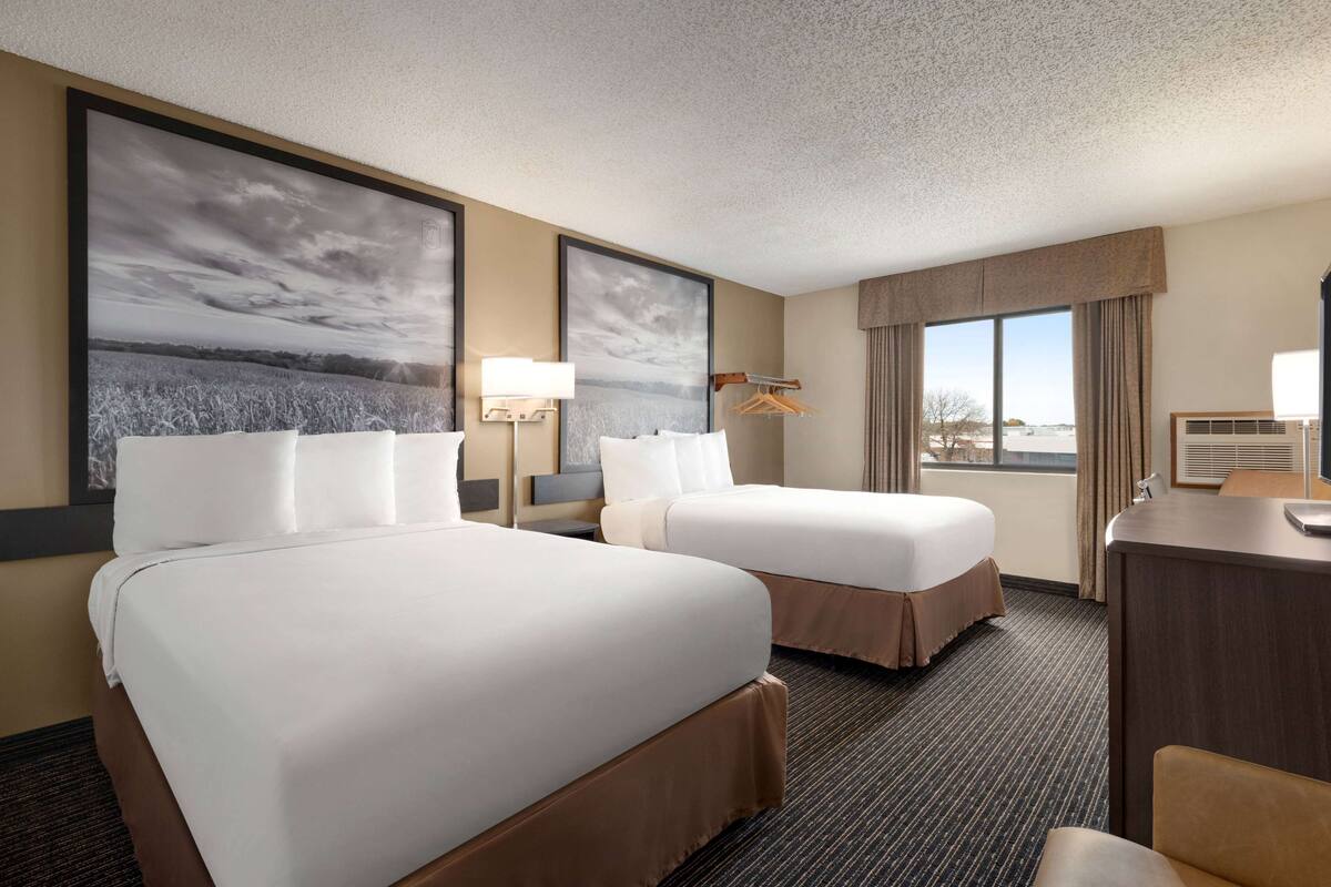 Habitación de hotel con dos camas, un escritorio, una silla, un ventanal y vista a la ciudad.