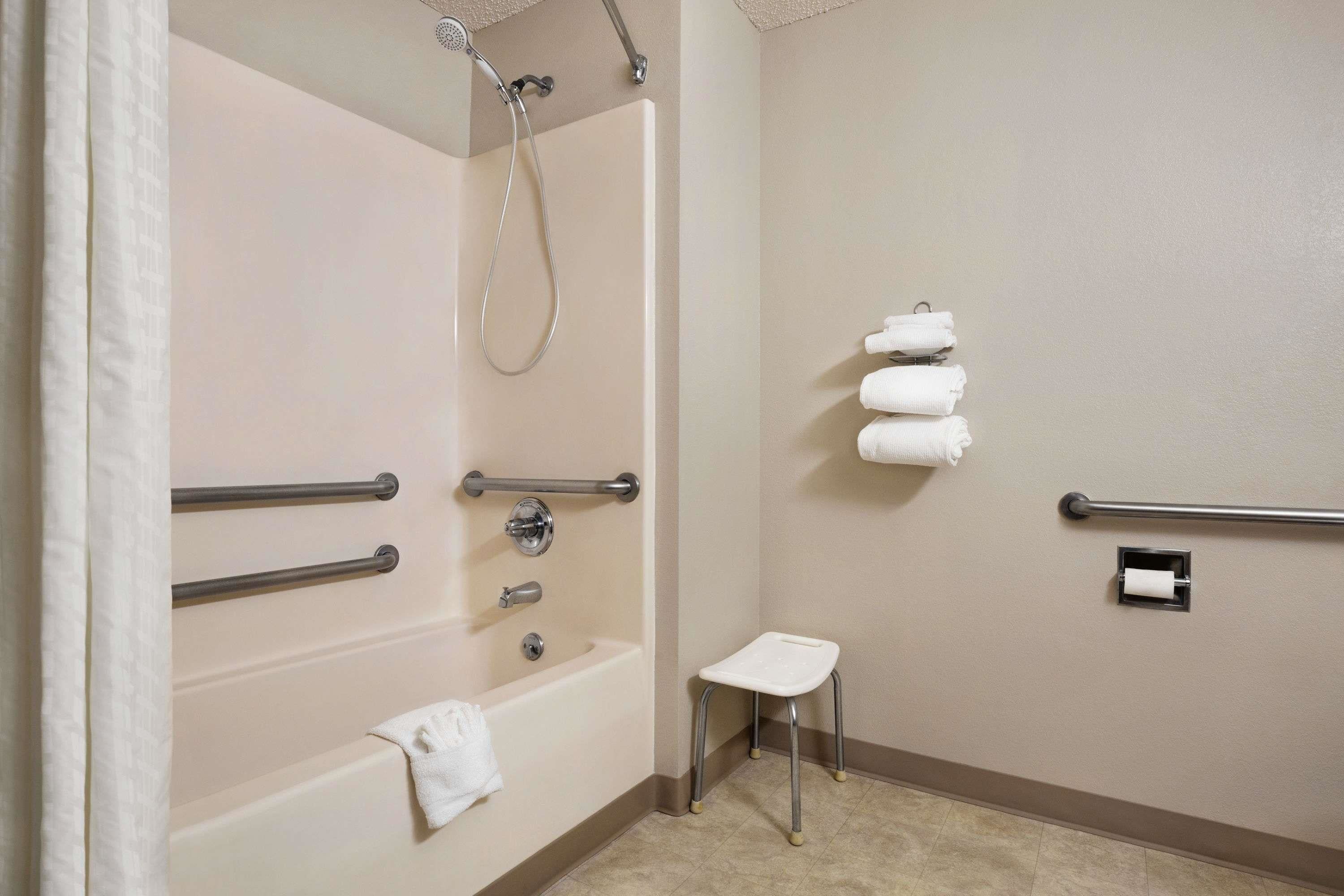 Une salle de bain équipée d’une baignoire, d’une douche, d’un porte-rouleau de papier toilette et d’un petit tabouret.