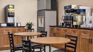 Une cuisine compacte équipée d’une machine à café, d’un réfrigérateur et d’un évier. On y trouve deux tables en bois accompagnées de chaises.