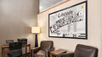 A hotel room with a desk, two leather chairs, a lamp, and a framed welcome sign.