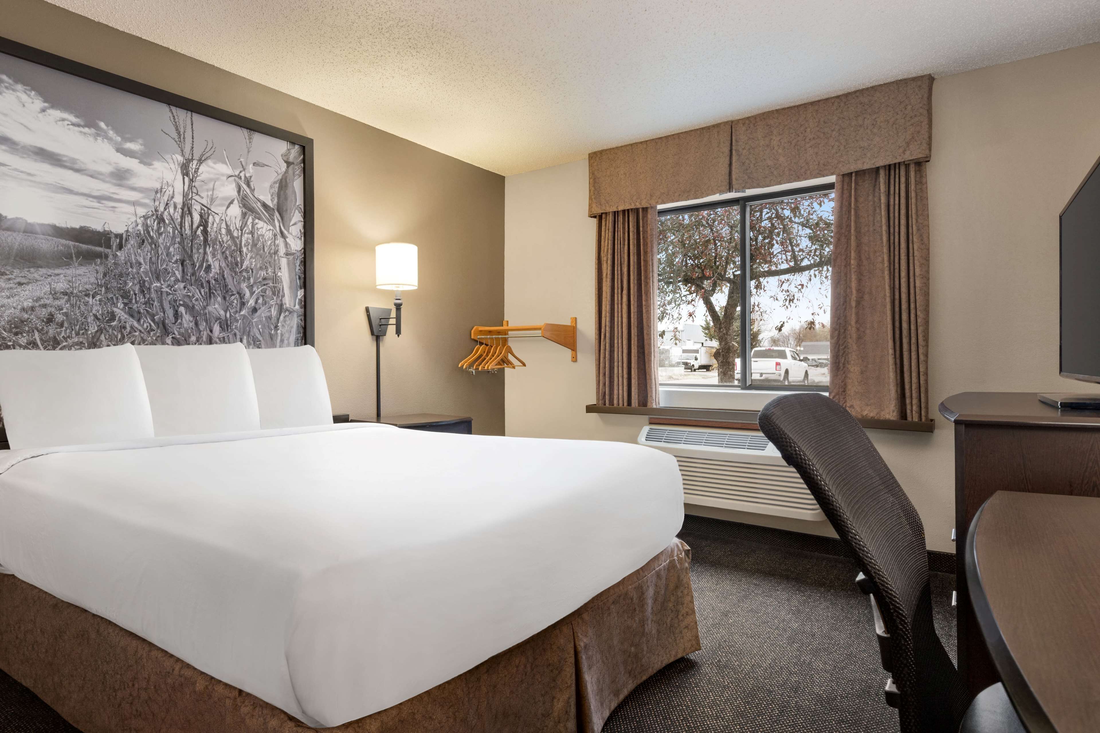 A hotel room with a large bed, a desk, a chair, a lamp, and a window with curtains.
