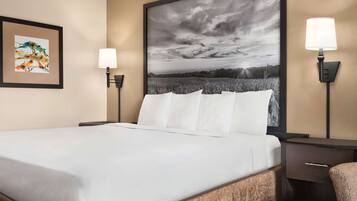 Habitación de hotel con una cama grande, dos lámparas de noche, una mesita y un cuadro en la pared.
