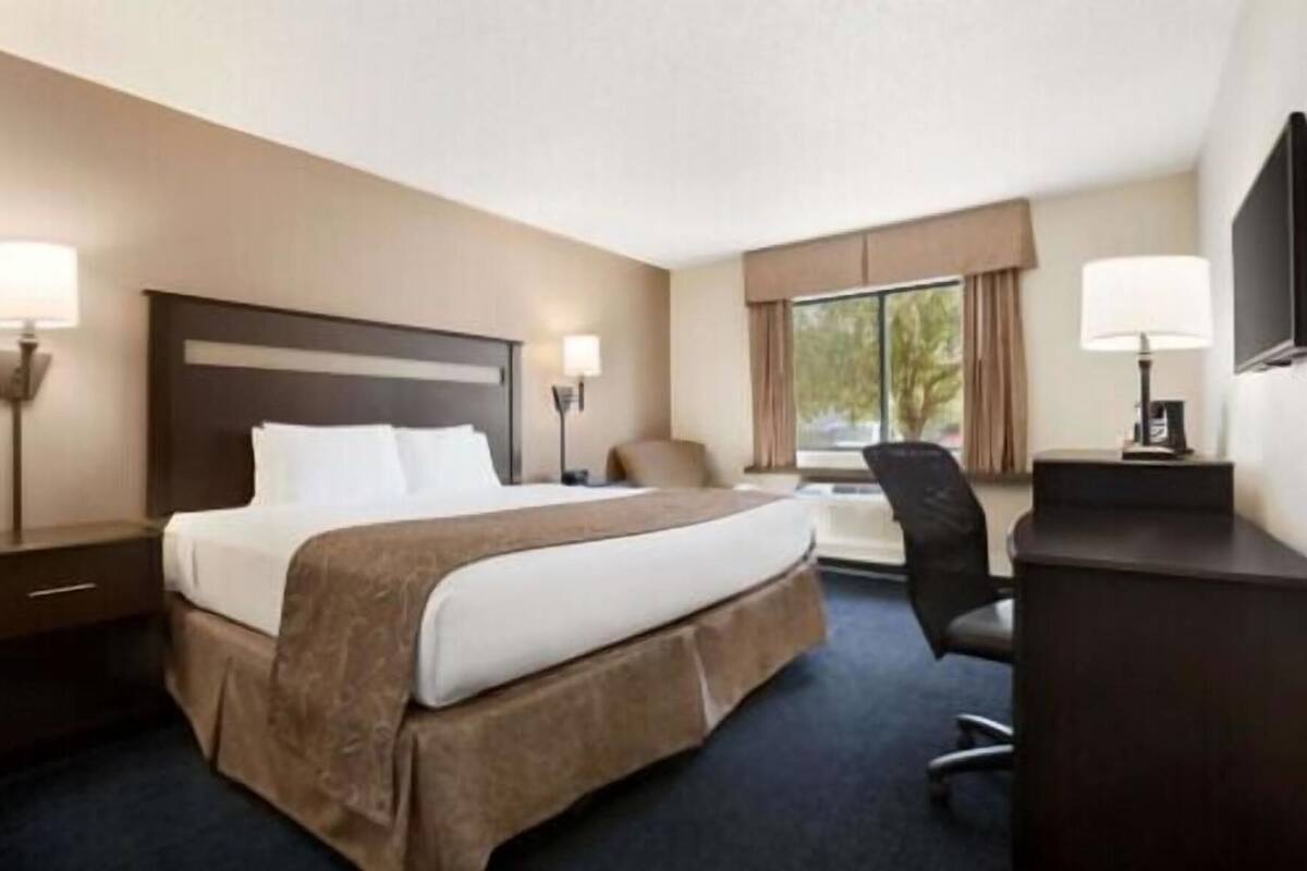 Habitación de hotel con una cama grande, un escritorio, dos lámparas y una ventana con cortinas.