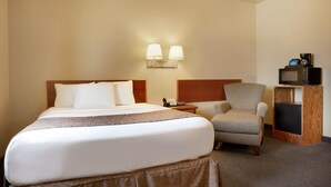 Quarto de hotel com uma cama grande, uma cadeira, uma escrivaninha com telefone e um micro-ondas.