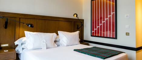 A hotel room with a large bed, a nightstand, a lamp, and a wall-mounted artwork.