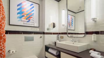 Un baño moderno con un lavamanos blanco, un espejo y una obra de arte enmarcada con un diseño abstracto y colorido.