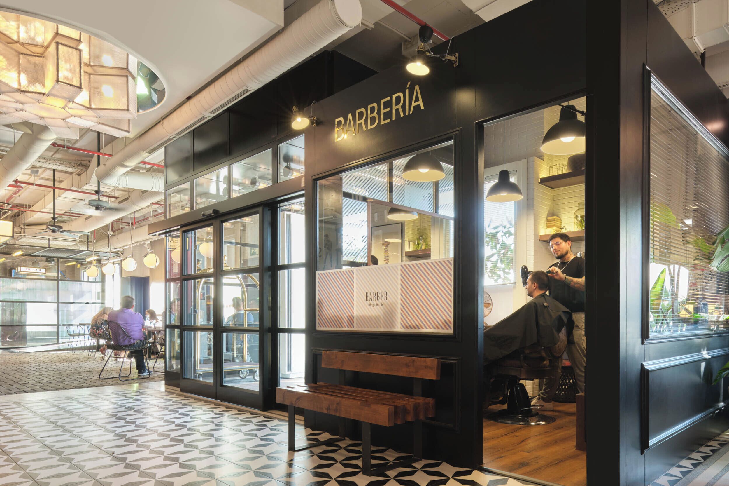 Una barbería con una decoración moderna, que incluye una banca en el exterior y un barbero atendiendo a un cliente.