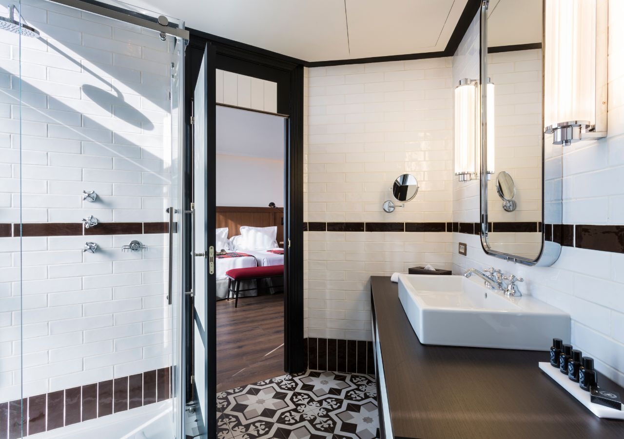 Un baño moderno con cabina de ducha de vidrio, un lavamanos blanco con espejo y piso estampado.