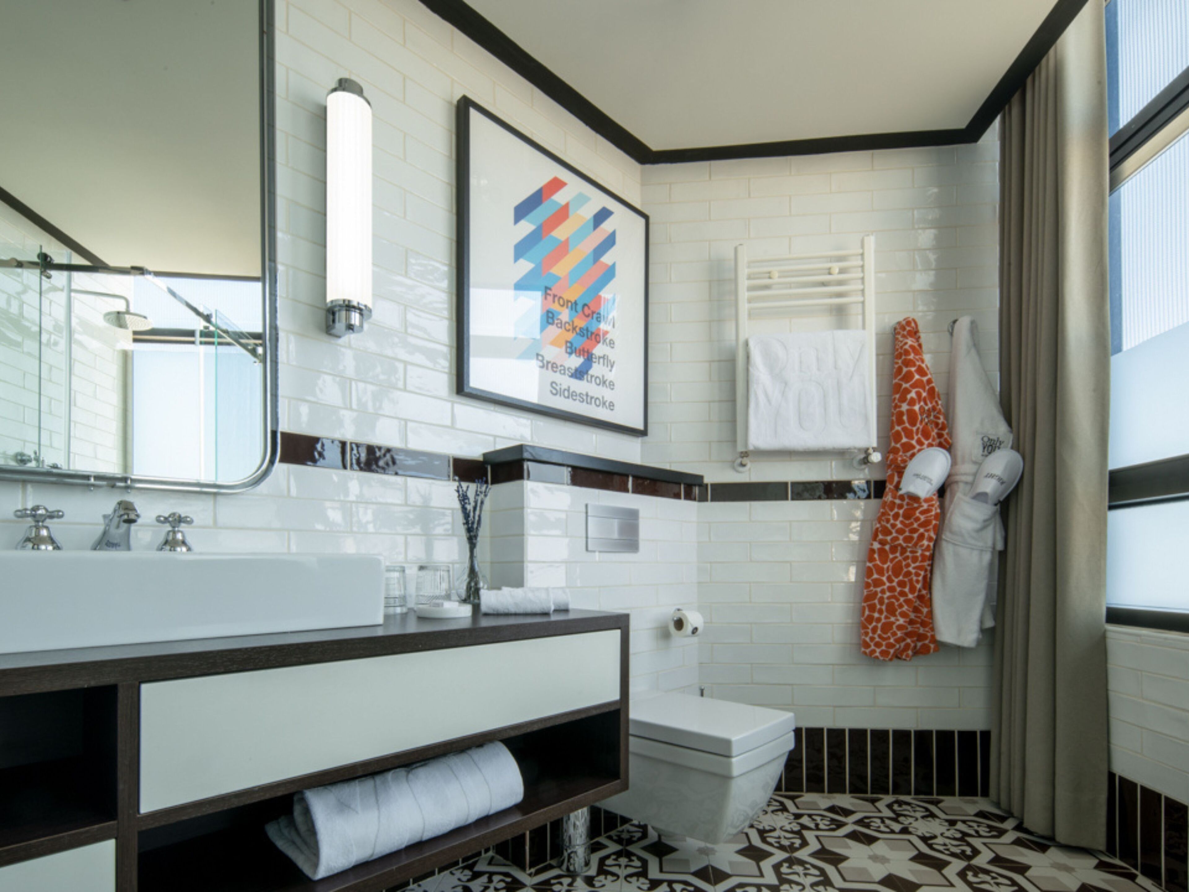 Un baño moderno con un lavamanos blanco, un espejo, una obra de arte enmarcada, un inodoro y un piso con diseño.
