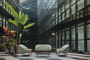 A modern interior with a glass facade, a seating area with a coffee table, and potted plants. - Only YOU Hotel Atocha (Madrid)