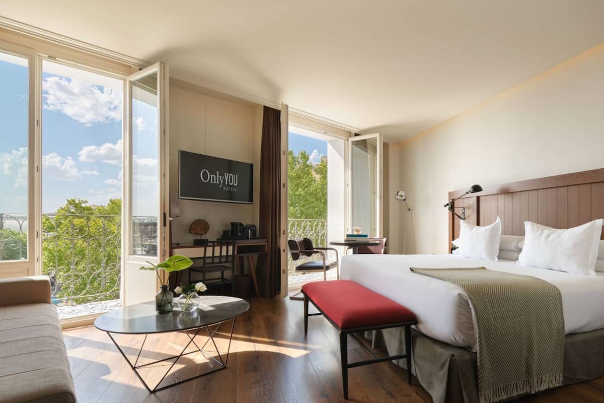 A hotel room with a bed, a desk, a chair, a TV, and a balcony with a view.