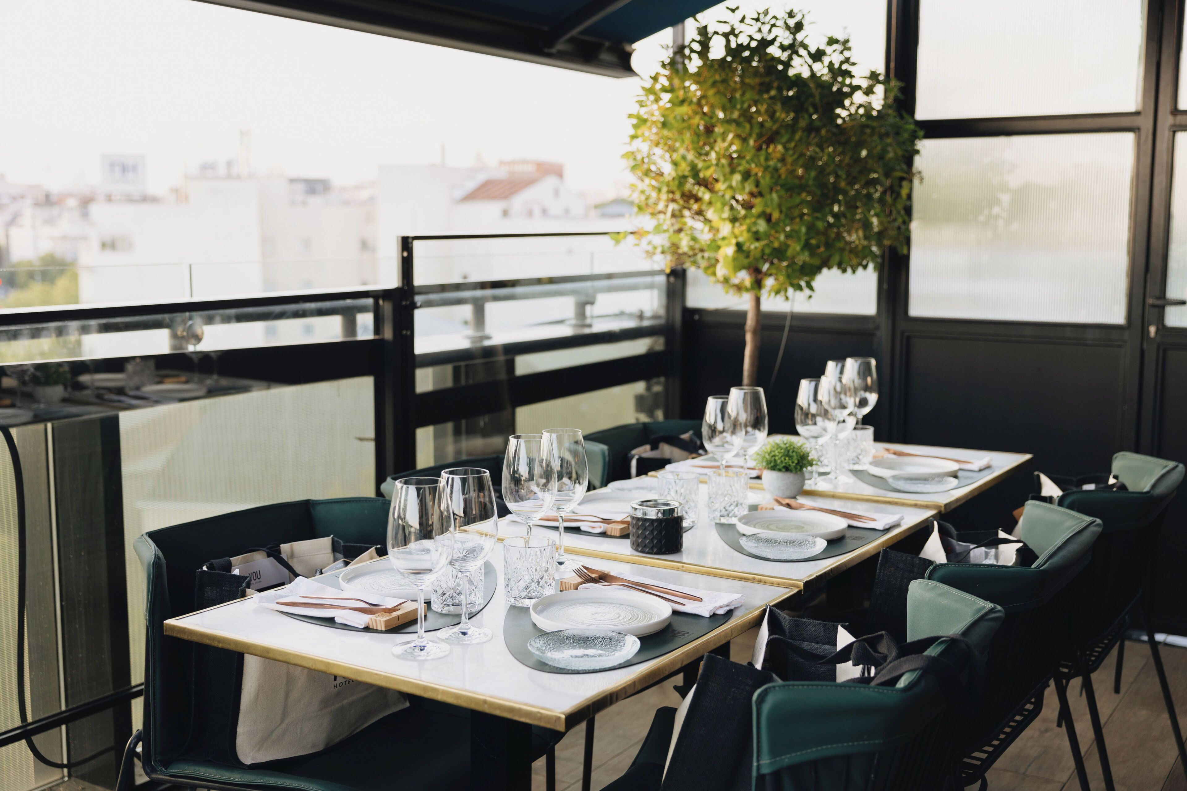 A restaurant table set with plates, glasses, and cutlery, overlooking a cityscape.
