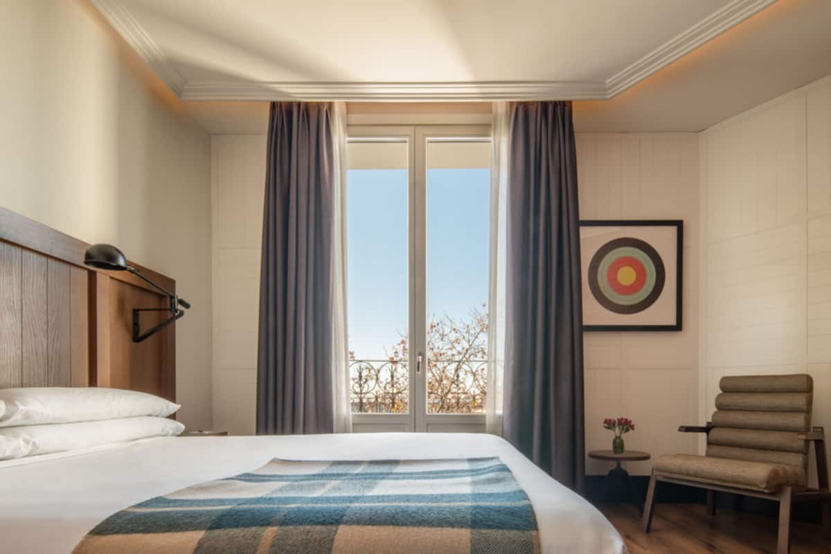 A hotel room with a large bed, a desk, a chair, and a window with curtains.