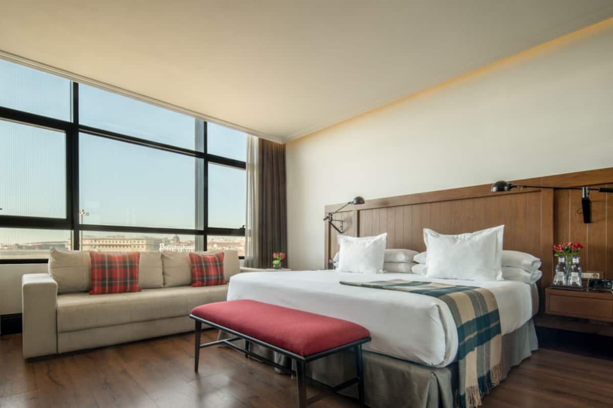 A hotel room with a large bed, a bench, a sofa, and a nightstand.