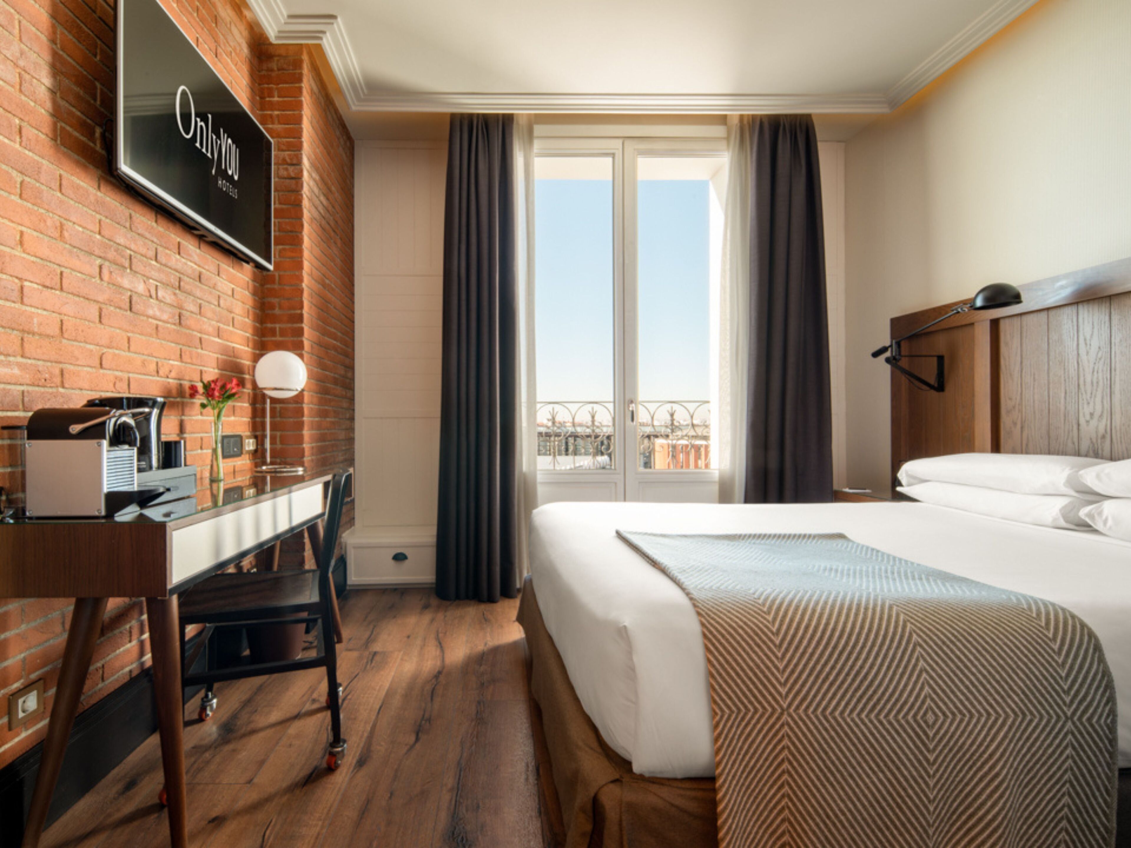 Ein Hotelzimmer mit Bett, Schreibtisch, Kaffeemaschine und Fernseher, der "Only You Hotels" anzeigt.