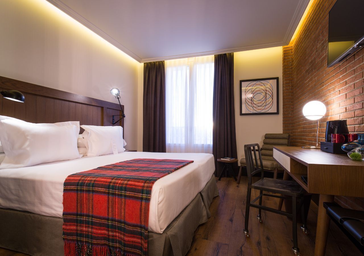 A hotel room with a bed, a desk, a chair, a coffee machine, and a television.