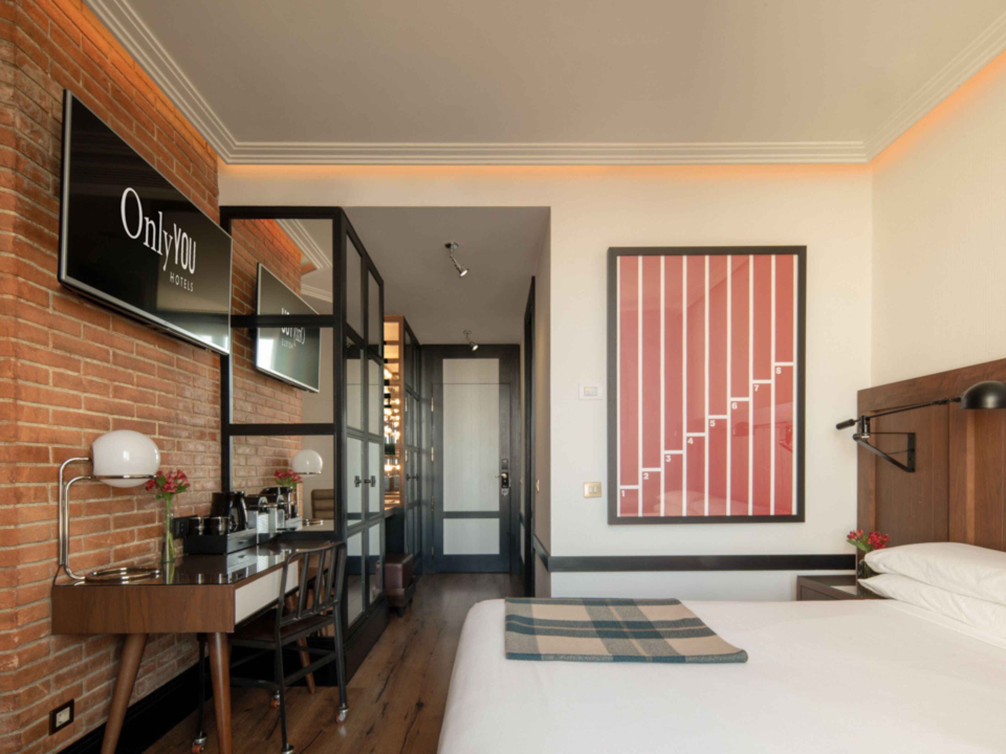 Habitaci ón de hotel con cama, escritorio, silla, espejo y una gran obra de arte en la pared.