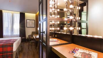 A hotel room with a bed, a desk with a magazine, and a mirror with lights.