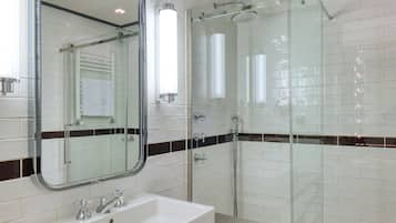 Un baño moderno con un espejo grande, un lavabo blanco, una cabina de ducha con mampara de vidrio y un salpicadero de azulejos.