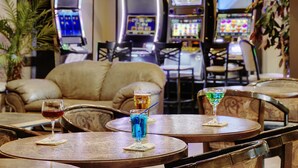 A bar area with two tables, each with a glass of drink, and three slot machines in the background. - Kindersley Inn (Kindersley)