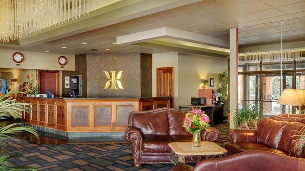 A lobby with a reception desk, leather sofas, a patterned carpet, and a chandelier. - Kindersley Inn (Kindersley)