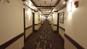 A hotel hallway with carpeted floors, framed pictures on the walls, and a fire alarm on the right. - Kindersley Inn (Kindersley)