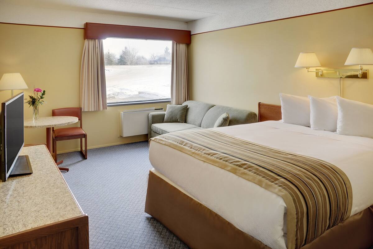 Een hotelkamer met een bed, een bureau met een computer, een stoel, een raam met gordijnen en een lamp.