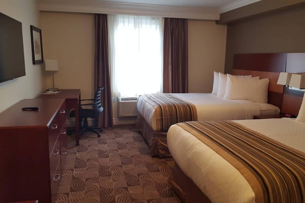 Een hotelkamer met twee bedden, een bureau, een stoel en een televisie aan de muur.