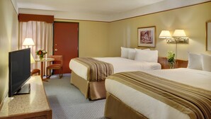 A hotel room with two beds, a desk with a television, a chair, and a table with a vase of flowers. - Kindersley Inn (Kindersley)