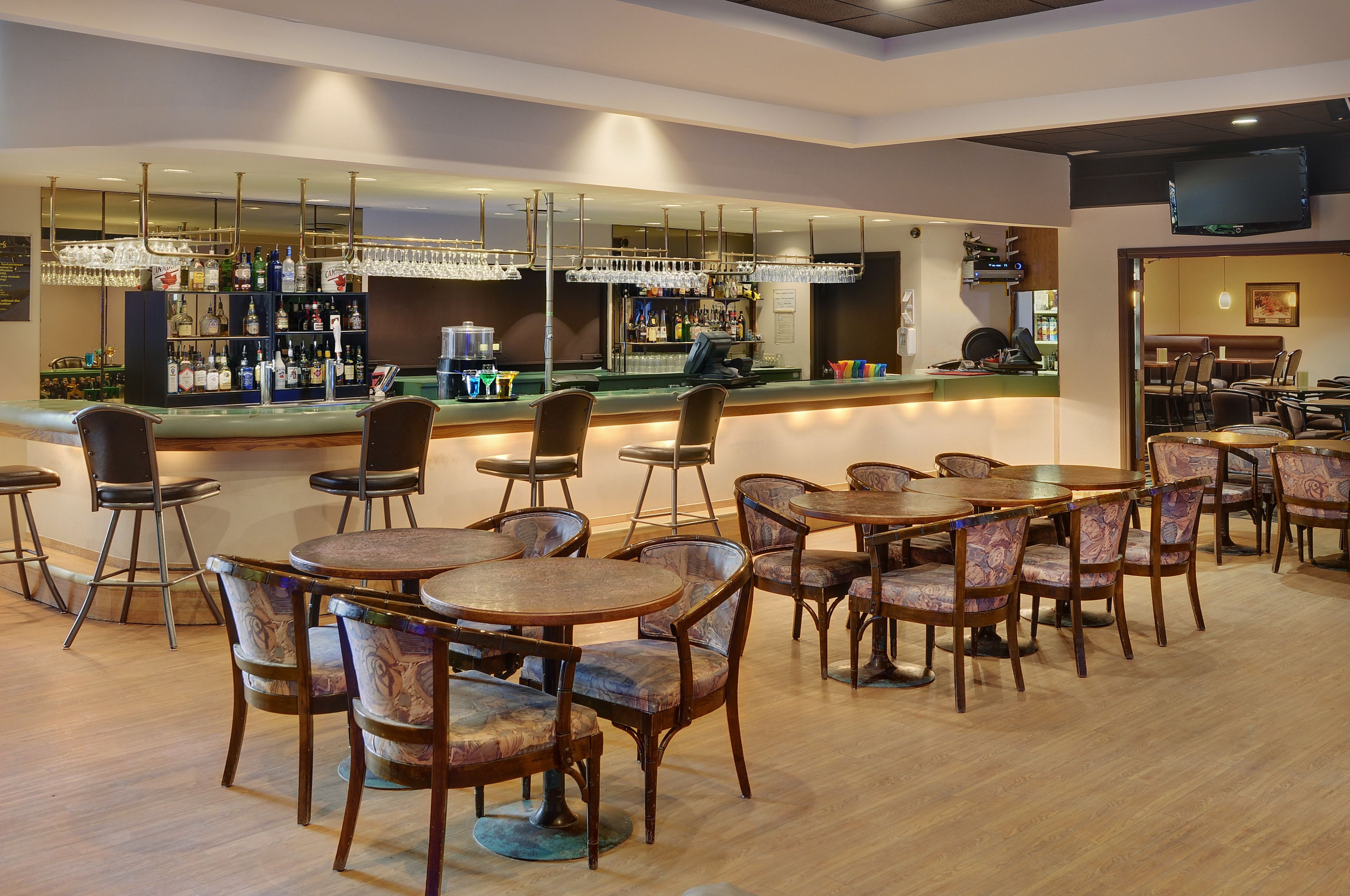 Zona de bar amb diverses opcions de seients, incloent taules rodones i tamborets, i una barra ben proveïda.