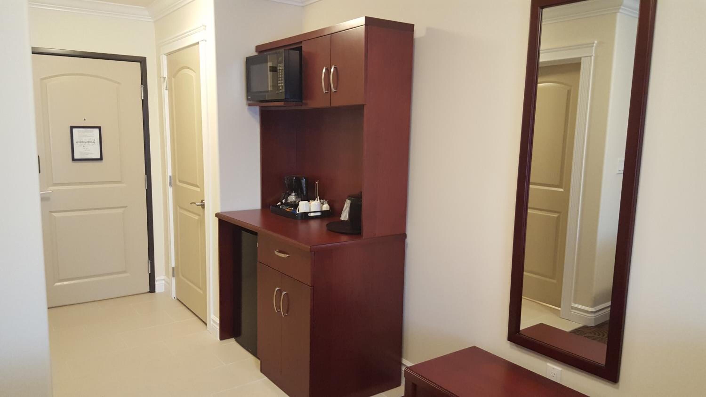 A hotel room with a wooden desk, a microwave, a coffee maker, and a large mirror.