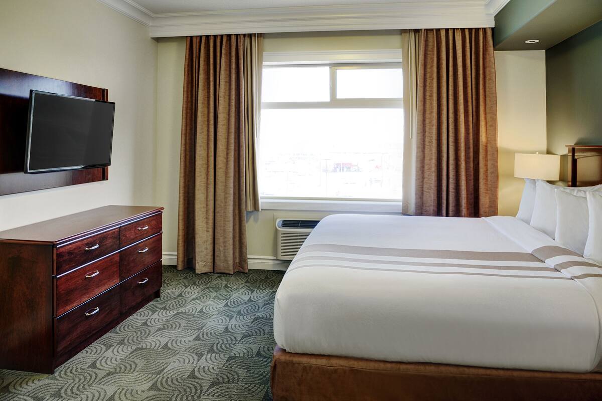Hotelkamer met een groot bed, een houten dressoir, een flatscreen televisie aan de muur en een raam met gordijnen.