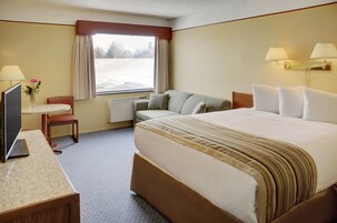 Habitación de hotel con una cama grande, un escritorio con computadora, una silla, una ventana con cortinas y una lámpara.