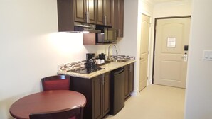 A compact kitchen with dark brown cabinets, a stainless steel sink, a microwave, and a coffee maker. - Kindersley Inn (Kindersley)