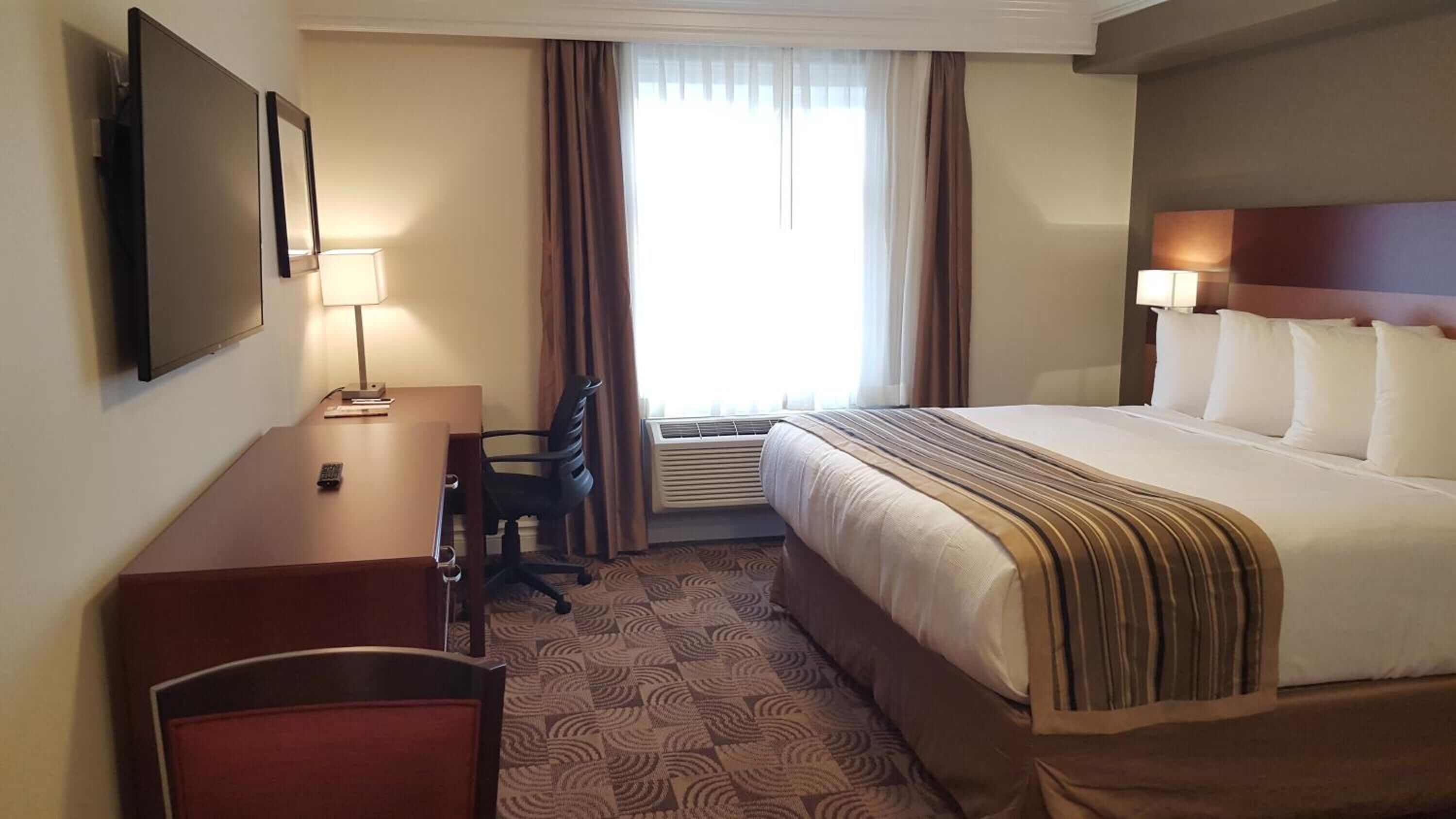 Una habitación de hotel con cama, escritorio, silla y televisor en la pared.