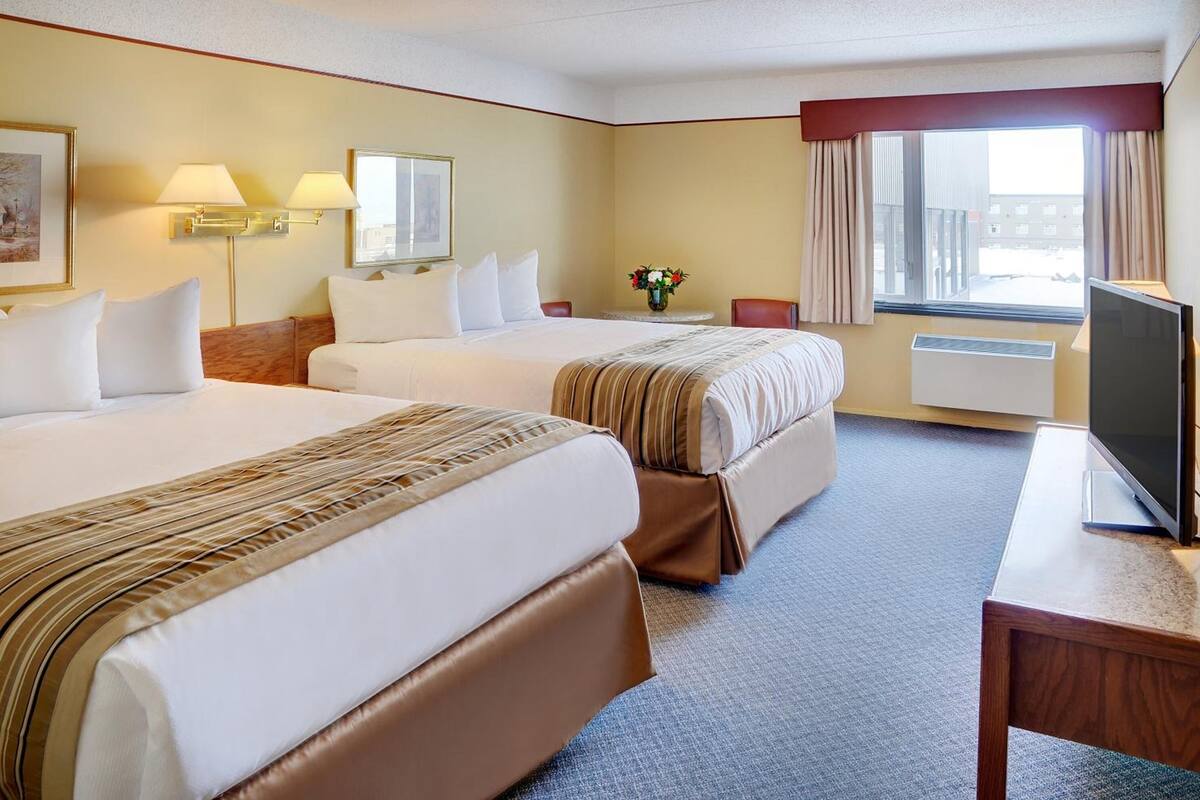 Een hotelkamer met twee bedden, een televisie, een bureau en een raam met gordijnen.