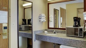 Casa de banho de hotel com lavatório, espelho, porta-toalhas, máquina de café e micro-ondas.
