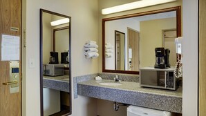 Casa de banho de hotel com bancada de granito, pia, espelho, máquina de café e micro-ondas.
