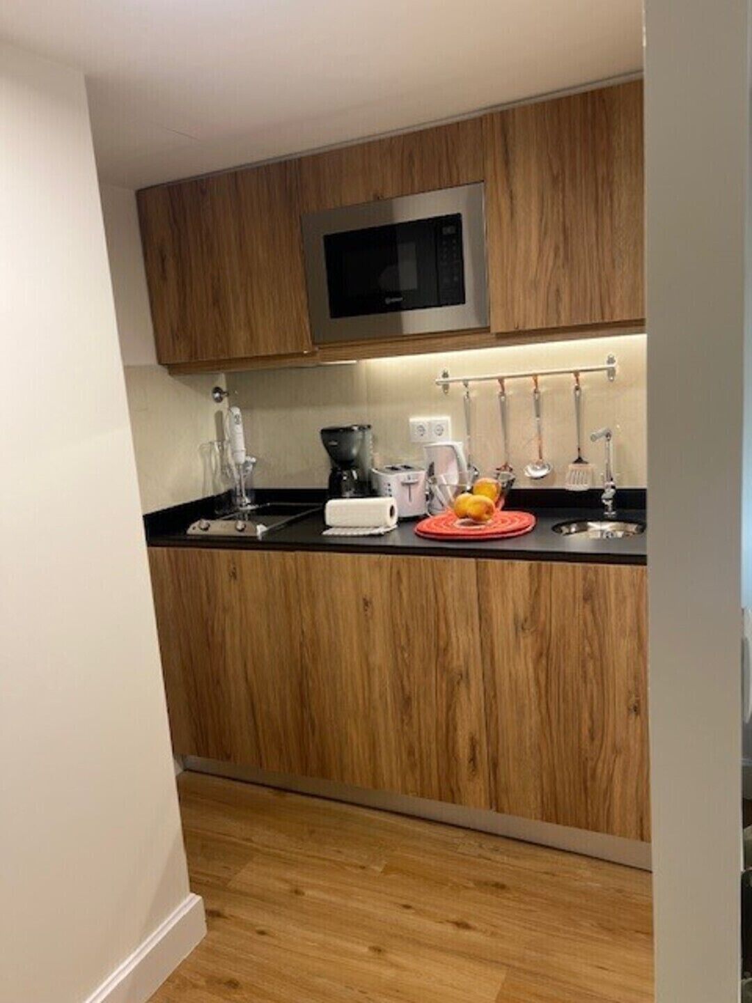 Een moderne keuken met houten kasten, een magnetron, een koffiezetapparaat en een fruitschaal.