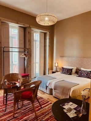 Une chambre d’hôtel avec un grand lit, une chaise, une petite table avec un vase et une lampe sur pied.