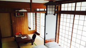 Una habitación japonesa tradicional con suelo de tatami, un escritorio de madera bajo, una cama con ropa blanca y puertas correderas shoji.